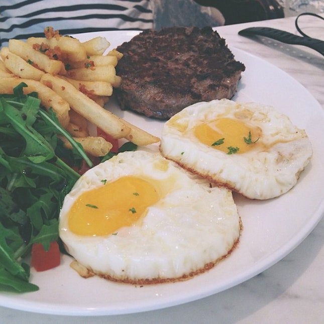 Beef patty with perfectly runny eggs and garlic fries and salad on the side